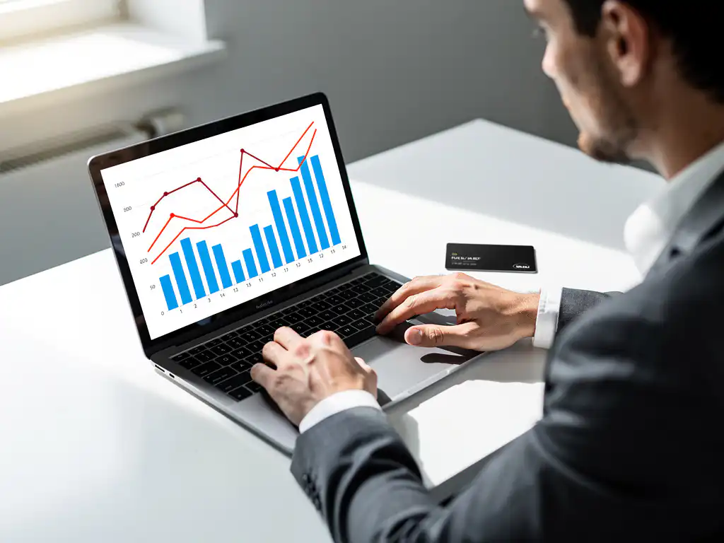 Vlootbeheerder analyseert brandstofkosten-dashboard op laptop met grafieklijnen en datatabellen, zwarte brandstofpas naast toetsenbord.