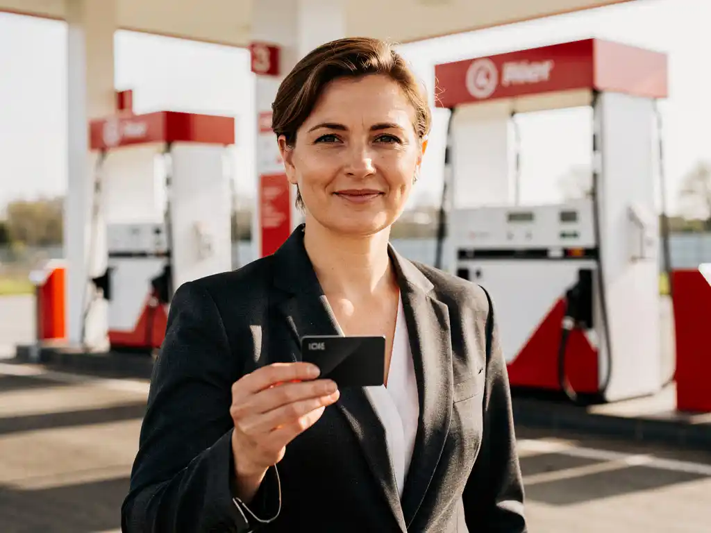 Zakenman in donker blazer houdt brandstofpas vast bij modern Nederlands tankstation met rode en witte luifels.