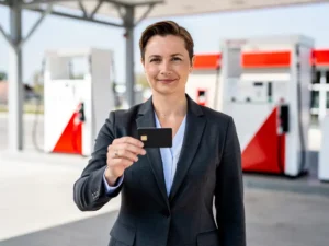 Zakelijke professional in donker blazer houdt brandstofpas vast bij modern Nederlands tankstation met witte en rode pompen.