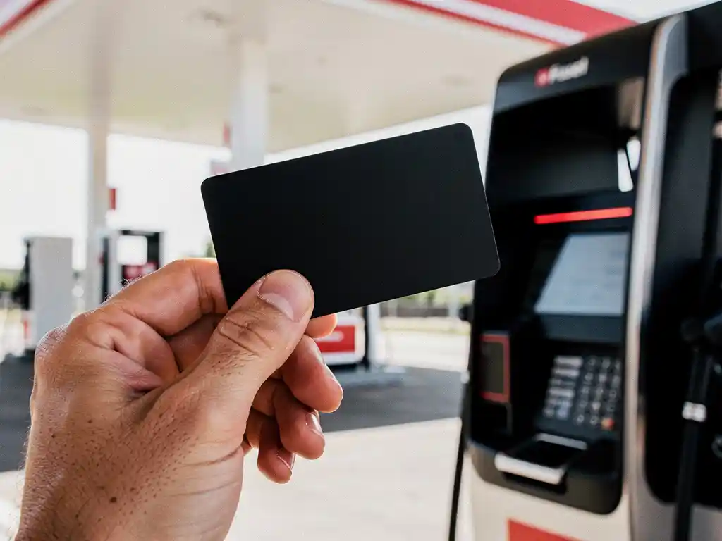 Zakenman houdt zwarte tankpas vast bij modern Nederlands tankstation met rood verlichte betaalterminal.
