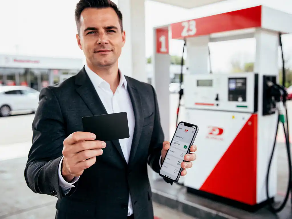 Zakenman met zwarte tankpas bij modern Nederlands tankstation, digitaal rittenregistratie-app zichtbaar op smartphone in andere hand.